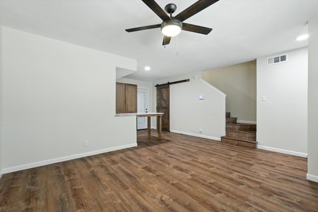 Unfurnished living room featuring a barn door, ceiling fan, stairway, wood finished floors, and recessed lighting | Image 8