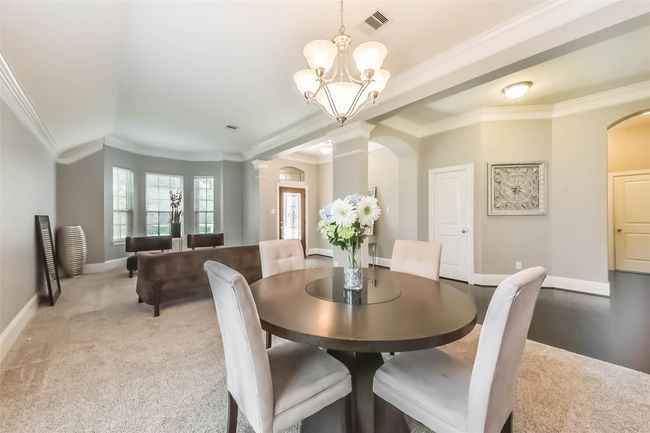 The dining/formal living provides a bright, welcoming entryway with dark hardwood floors and elegant archways. A formal dining area with large windows and plush seating is visible to the right, providing ample natural light and a cozy atmosphere. | Image 6