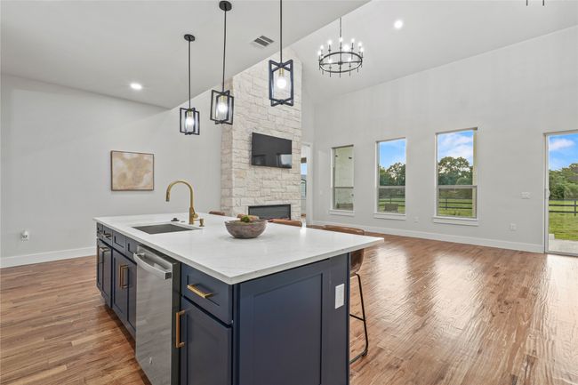 Kitchen with high vaulted ceiling, open floor plan, light wood-style floors, a stone fireplace, and a center island with sink | Image 12