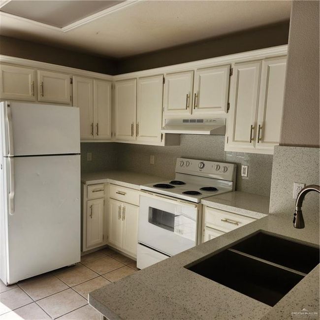 Kitchen with fridge, extractor fan, range, light tile patterned floors, and white cabinets | Image 4