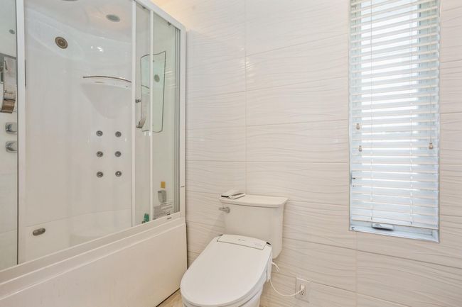 Bathroom featuring a shower with door, a washtub, tile walls, and toilet | Image 7