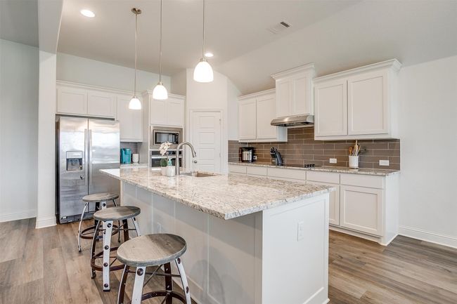 Kitchen with stainless steel appliances, baseboards, decorative backsplash, white cabinets, and lofted ceiling | Image 12