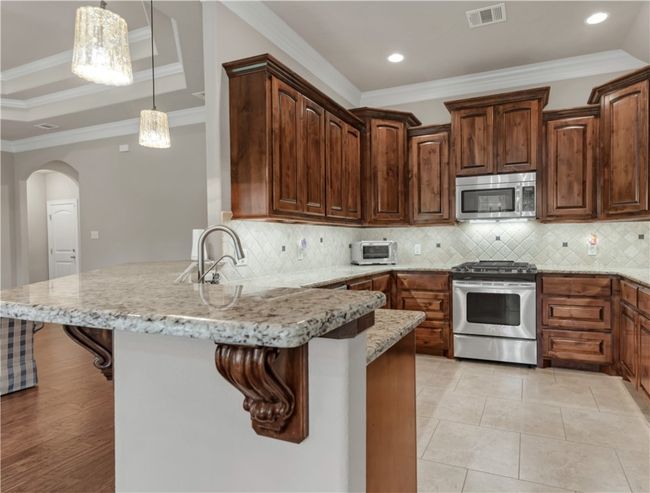 Kitchen with appliances with stainless steel finishes, ornamental molding, a kitchen breakfast bar, a peninsula, and arched walkways | Image 13
