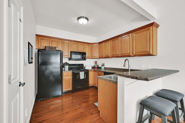 Kitchen featuring a breakfast bar, a peninsula, a sink, black appliances, and dark wood-type flooring | Image 25