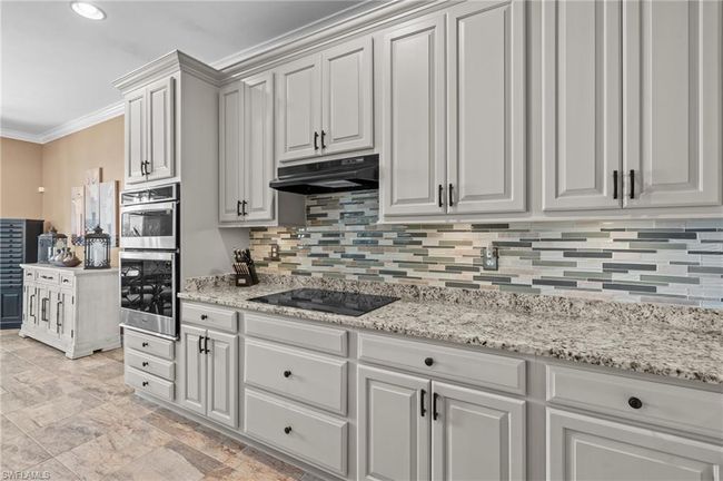 Kitchen featuring black electric stovetop, under cabinet range hood, tasteful backsplash, ornamental molding, and stainless steel double oven | Image 22