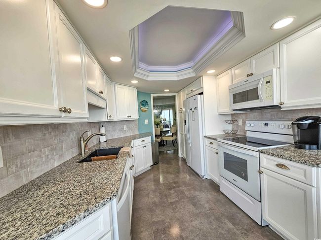 Kitchen with white appliances, ornamental molding, white cabinets, a raised ceiling, and recessed lighting | Image 20