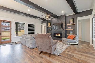 Living room with beam ceiling, a large fireplace, ceiling fan, wood-type flooring, and built in features | Image 3