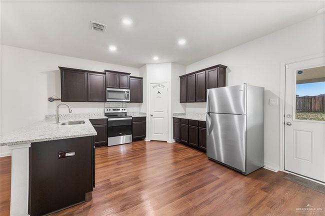 Kitchen featuring appliances with stainless steel finishes, a peninsula, a sink, dark wood-type flooring, and dark brown cabinets | Image 9