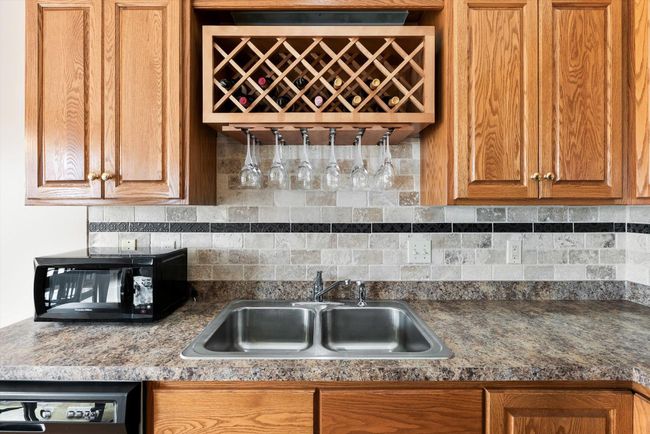 Charming sink area with a built-in wood wine rack and glass holder, tiled backsplash, and oak cabinetry for warm, classic style. | Image 12