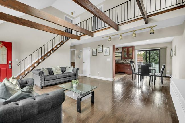 Living area with dark wood finished floors, stairway, rail lighting, beam ceiling, and baseboards | Image 4