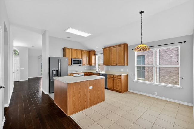 Kitchen with stainless steel appliances, vaulted ceiling, light countertops, a kitchen island, and brown cabinetry | Image 7