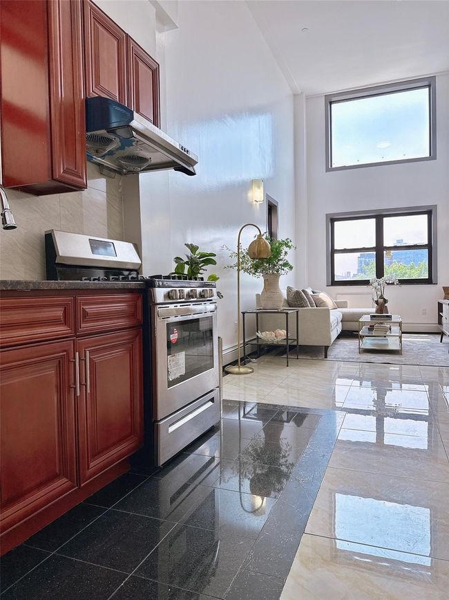 Kitchen with stainless steel gas range, ventilation hood, a high ceiling, reddish brown cabinets, and dark countertops | Image 6
