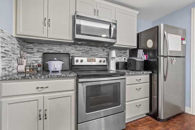 Kitchen featuring appliances with stainless steel finishes, dark stone countertops, decorative backsplash, and dark wood-style floors | Image 13