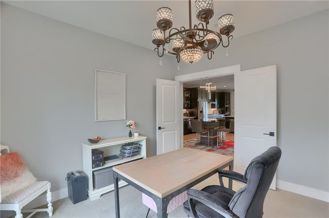 This inviting den with French door access offers a perfect work-from-home setup, featuring custom built-ins, elegant display cabinets, and a statement chandelier—all framed by a large window overlooking the charming townhome community. | Image 17