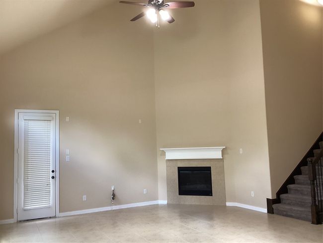 Unfurnished living room featuring high vaulted ceiling, tile patterned flooring, a ceiling fan, a fireplace, and stairway | Image 4