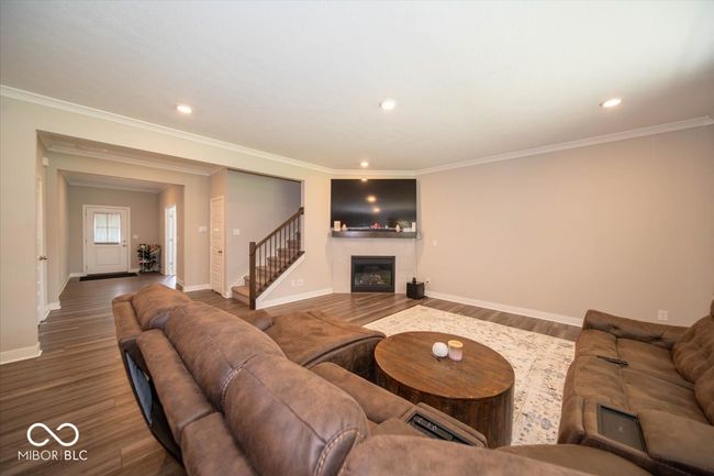 living room with wood finished floors, a glass covered fireplace, stairs, ornamental molding, and recessed lighting | Image 8