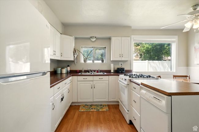 Kitchen featuring white appliances, dark countertops, ceiling fan, light wood finished floors, and white cabinets | Image 6