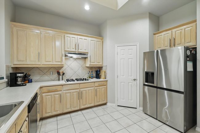 Kitchen featuring decorative backsplash, light brown cabinetry, appliances with stainless steel finishes, light countertops, and under cabinet range hood | Image 12
