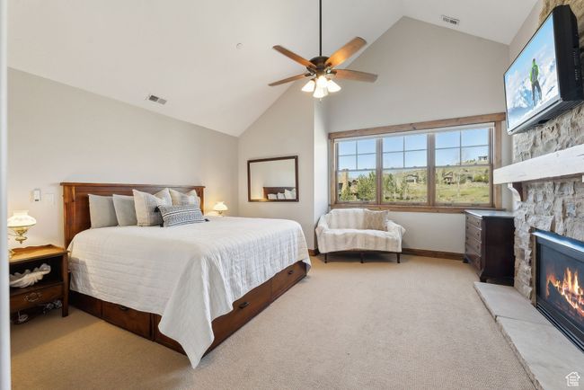 Bedroom with light carpet, high vaulted ceiling, a stone fireplace, a ceiling fan, and visible vents | Image 15