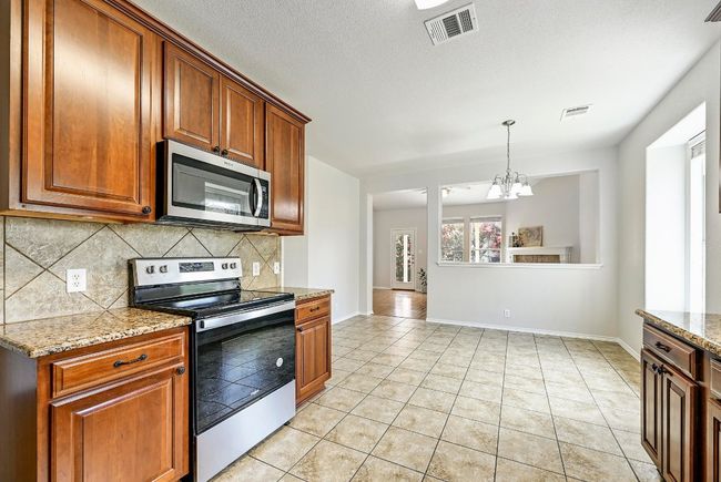Kitchen with stainless steel appliances, backsplash, a chandelier, light tile patterned flooring, and light stone countertops | Image 8