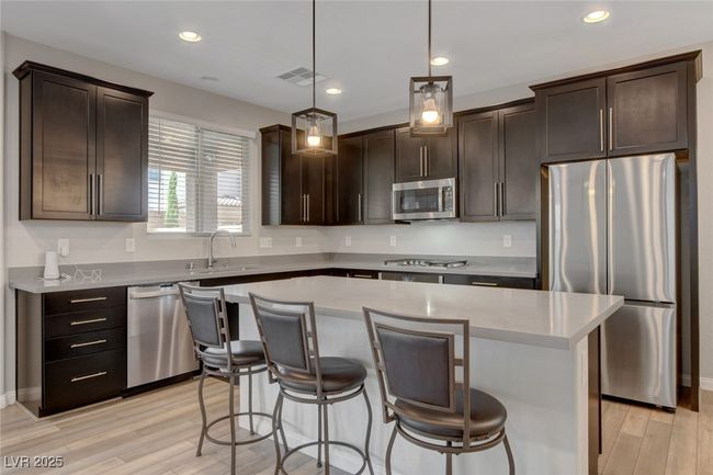 Kitchen featuring stainless steel appliances, a kitchen island, light wood finished floors, dark brown cabinets, and recessed lighting | Image 16