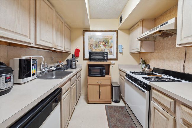 Kitchen with white appliances, under cabinet range hood, light brown cabinetry, light countertops, and a textured ceiling | Image 17