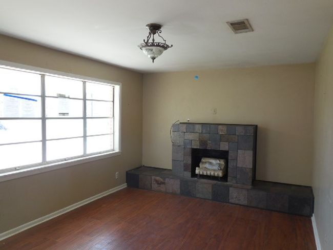 Unfurnished living room featuring visible vents, baseboards, a fireplace with raised hearth, and wood finished floors | Image 4