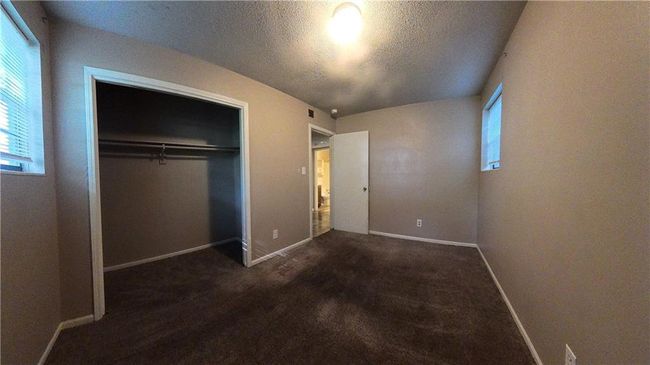 Unfurnished bedroom featuring a textured ceiling, a closet, and dark colored carpet | Image 4