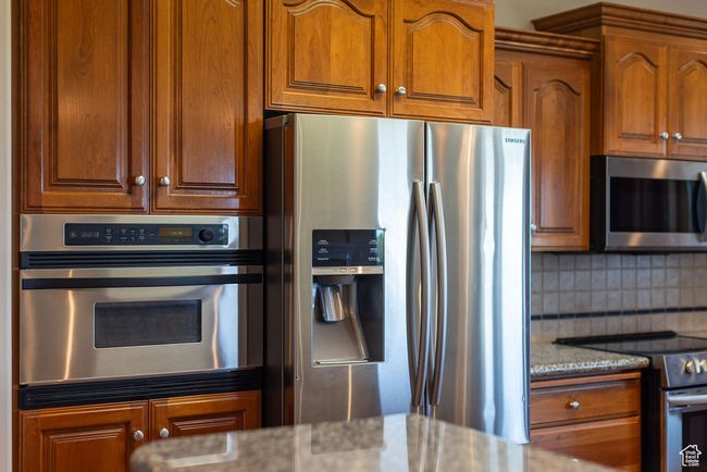 Kitchen featuring appliances with stainless steel finishes, light stone countertops, decorative backsplash, and brown cabinets | Image 10