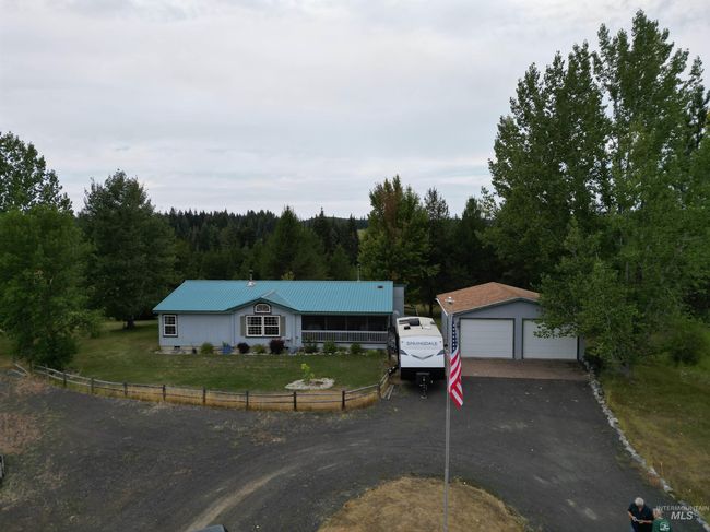 Ranch-style house featuring an outbuilding, a detached garage, a metal roof, and a forest view | Image 13