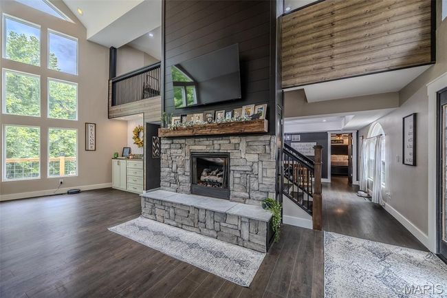 Unfurnished living room with a stone fireplace, high vaulted ceiling, wood finished floors, stairs, and plenty of natural light | Image 8