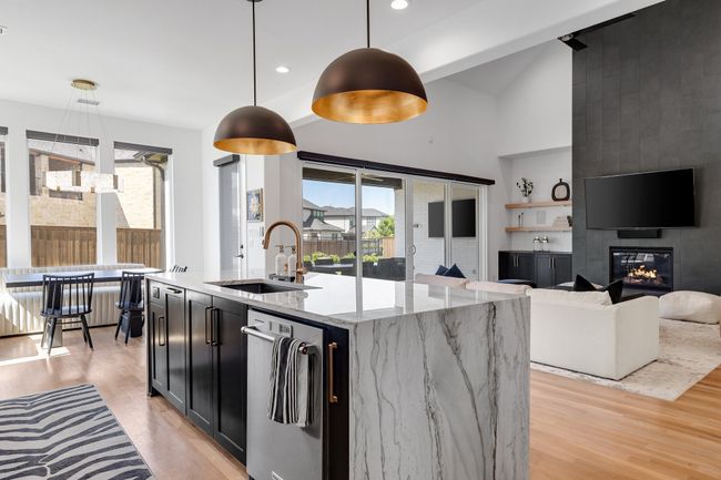Kitchen featuring a sink, light wood-type flooring, dark cabinets, hanging light fixtures, and light stone counters | Image 15