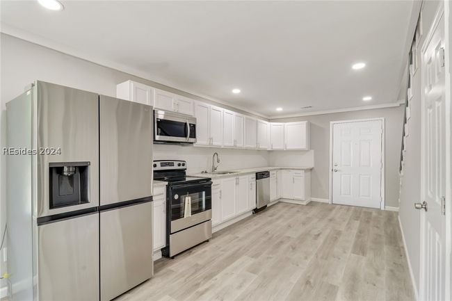 Kitchen with white cabinetry, stainless steel appliances, crown molding, light wood-type flooring, and sink. Connecting door virtually enhanced | Image 31