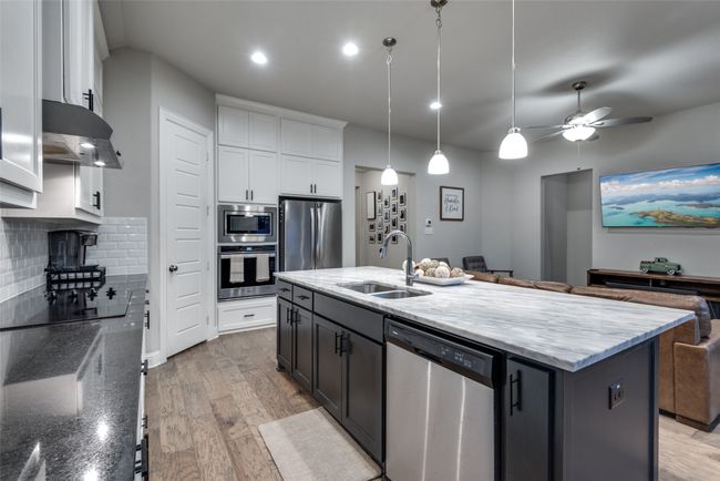 Kitchen with a sink, tasteful backsplash, white cabinetry, under cabinet range hood, and appliances with stainless steel finishes | Image 7