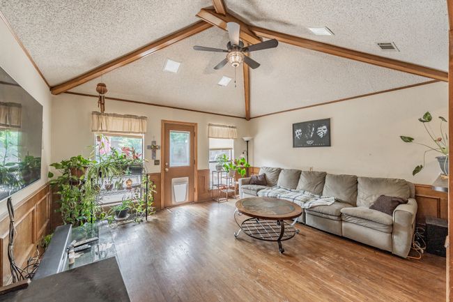 Living room with a wainscoted wall, a textured ceiling, wood finished floors, and ceiling fan | Image 5