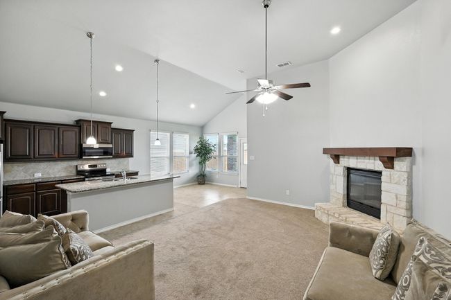Living area with recessed lighting, high vaulted ceiling, light carpet, a ceiling fan, and a stone fireplace | Image 4