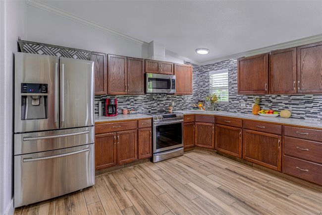 Kitchen featuring crown molding, light countertops, tasteful backsplash, light wood finished floors, and stainless steel appliances | Image 7