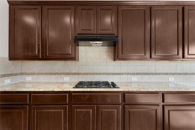 Kitchen with under cabinet range hood, dark brown cabinets, black gas stovetop, and tasteful backsplash | Image 27