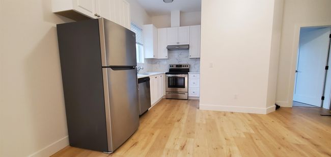 Kitchen featuring light wood-style flooring, white cabinetry, appliances with stainless steel finishes, and under cabinet range hood | Image 37
