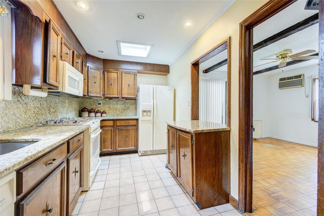 Kitchen featuring white appliances, tasteful backsplash, a skylight, a wall mounted air conditioner, and brown cabinets | Image 14