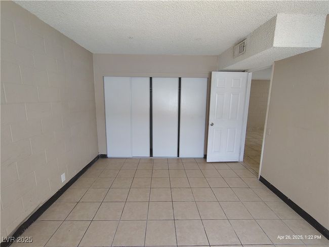 Unfurnished bedroom featuring a textured ceiling, visible vents, concrete block wall, and a closet | Image 7