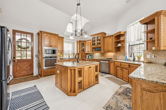 Kitchen with appliances with stainless steel finishes, open shelves, brown cabinetry, backsplash, and a chandelier | Image 5