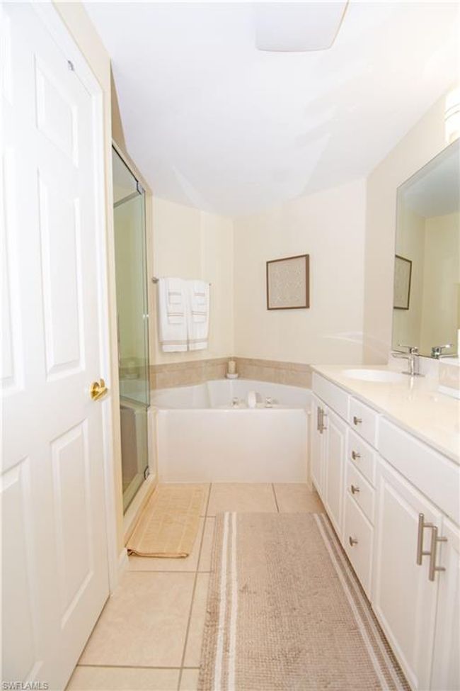Updated primary bathroom features a double vanity, water closet, soaking tub and custom tiled shower. | Image 19