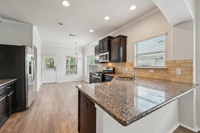 Kitchen with stainless steel appliances, stone counters, a sink, light wood-style flooring, and dark brown cabinets | Image 12