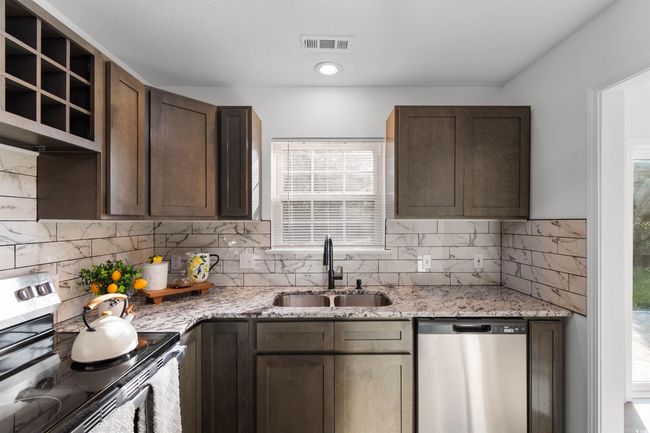 Kitchen with stainless steel appliances, decorative backsplash, light stone counters, light wood-type flooring, and dark brown cabinets | Image 6