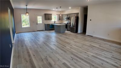 Kitchen with light wood-type flooring, hanging light fixtures, a kitchen island, gray cabinetry, and stainless steel appliances | Image 2