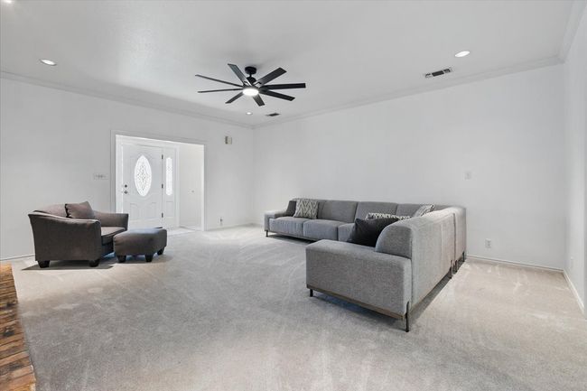 Carpeted living room featuring a ceiling fan, baseboards, crown molding, and recessed lighting | Image 10