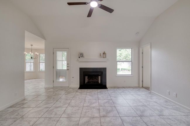 Unfurnished living room with vaulted ceiling, plenty of natural light, a ceiling fan, a fireplace, and a chandelier | Image 5