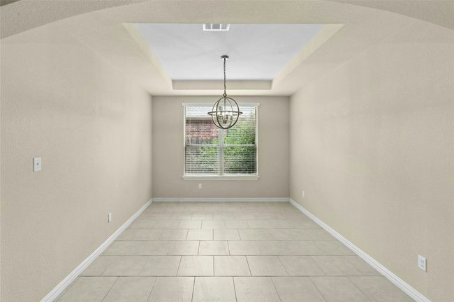 Spare room with a chandelier, a tray ceiling, baseboards, and light tile patterned flooring | Image 4