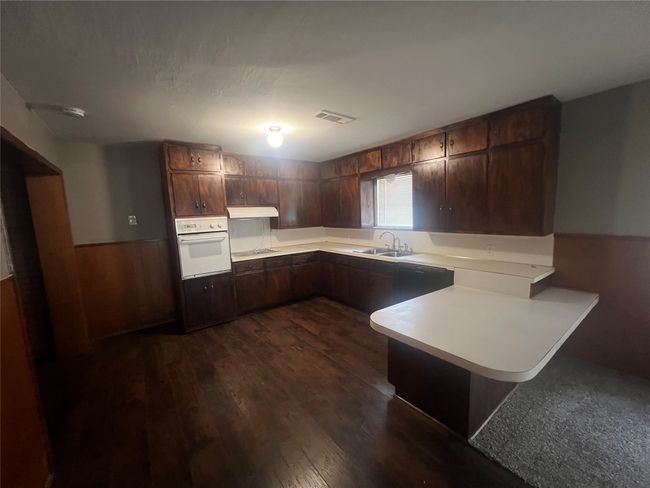 Kitchen with white oven, a peninsula, light countertops, dark wood-type flooring, and wainscoting | Image 13